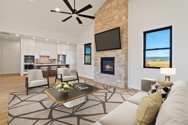 living room featuring visible vents, light wood-style floors, a fireplace, and high vaulted ceiling