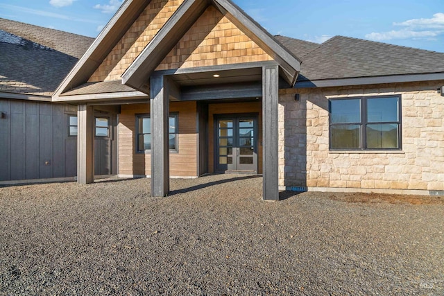 rear view of property featuring french doors, stone siding, and roof with shingles