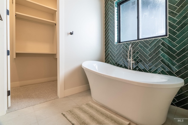 full bathroom with tile patterned flooring, tile walls, a freestanding tub, and baseboards