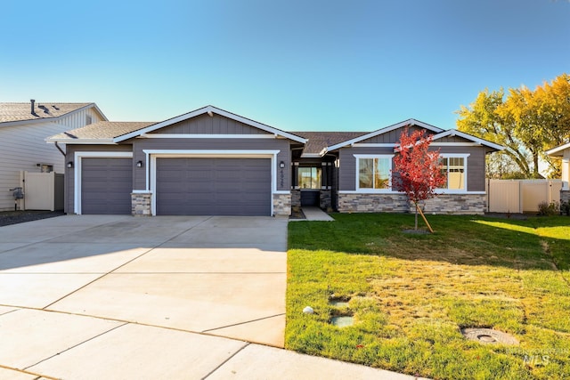 craftsman-style house featuring a front lawn, stone siding, an attached garage, and fence