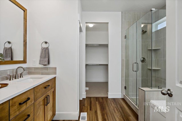 full bath featuring a shower stall, visible vents, wood finished floors, vanity, and a walk in closet