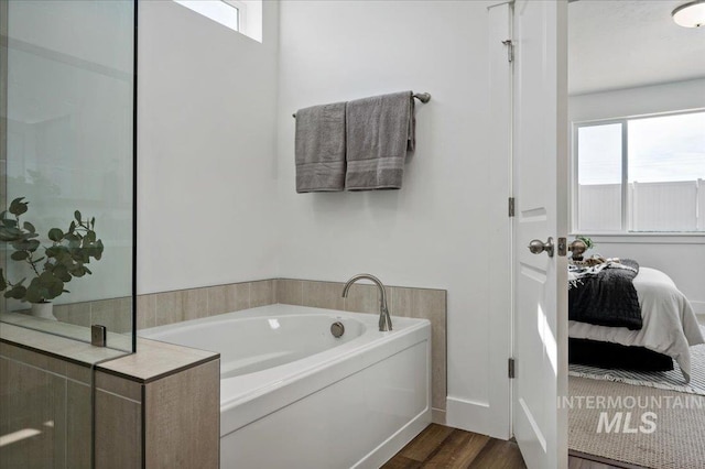 full bath featuring a bath, a healthy amount of sunlight, wood finished floors, and ensuite bath