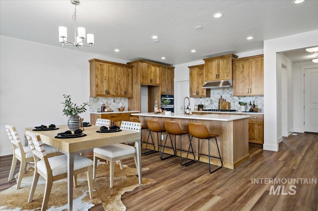 kitchen with light countertops, dark wood finished floors, brown cabinets, and tasteful backsplash