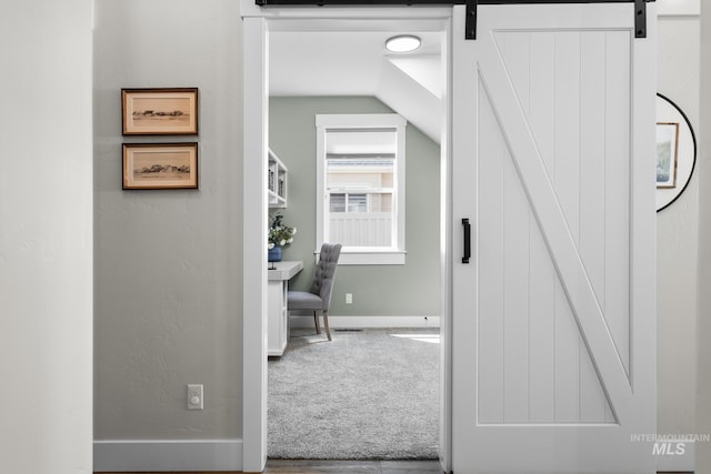 hall with visible vents, vaulted ceiling, a barn door, baseboards, and carpet floors