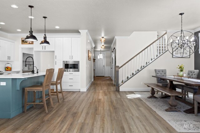 kitchen featuring light wood-type flooring, a sink, light countertops, stainless steel microwave, and ornamental molding