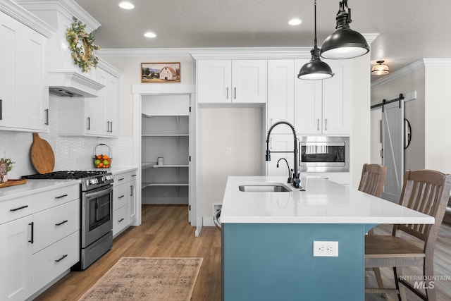 kitchen featuring ornamental molding, a center island with sink, a sink, appliances with stainless steel finishes, and backsplash