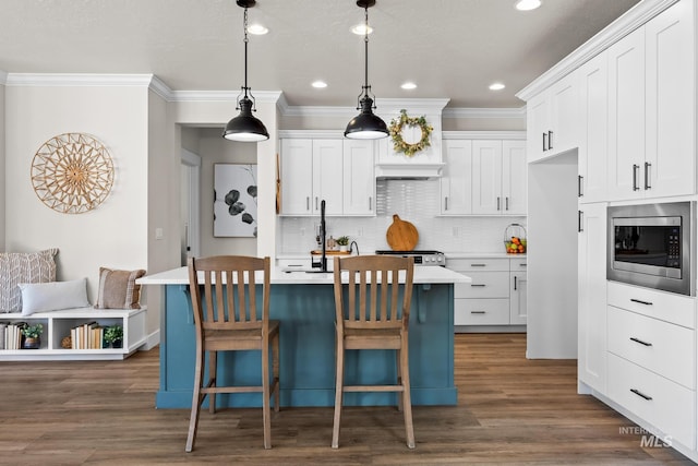 kitchen with crown molding, light countertops, stainless steel microwave, and backsplash