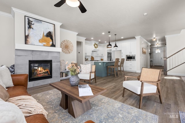 living room with light wood-style floors, a ceiling fan, a fireplace, and ornamental molding