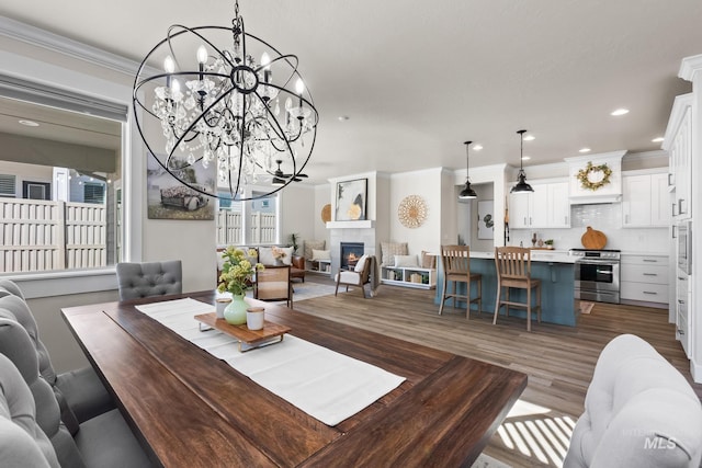 dining room featuring a chandelier, a tiled fireplace, recessed lighting, wood finished floors, and ornamental molding