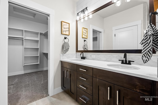 bathroom with a sink, a walk in closet, baseboards, and double vanity