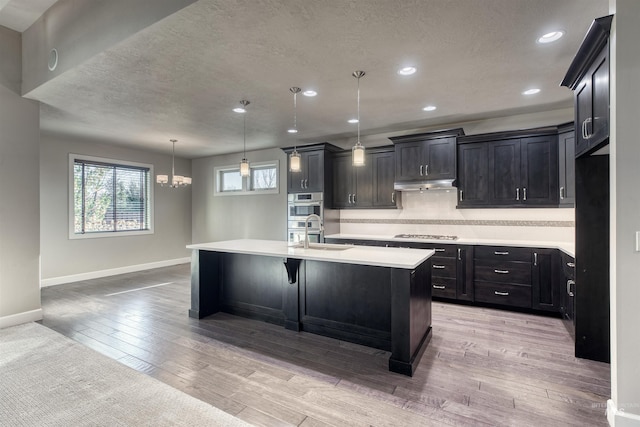 kitchen featuring stainless steel gas cooktop, light hardwood / wood-style flooring, decorative light fixtures, decorative backsplash, and a center island with sink