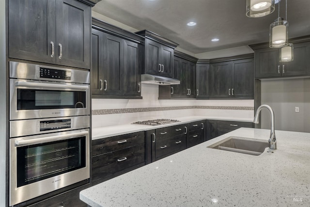 kitchen featuring light stone countertops, appliances with stainless steel finishes, backsplash, sink, and pendant lighting