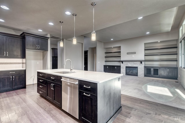 kitchen featuring light wood-type flooring, a kitchen island with sink, sink, dishwasher, and hanging light fixtures