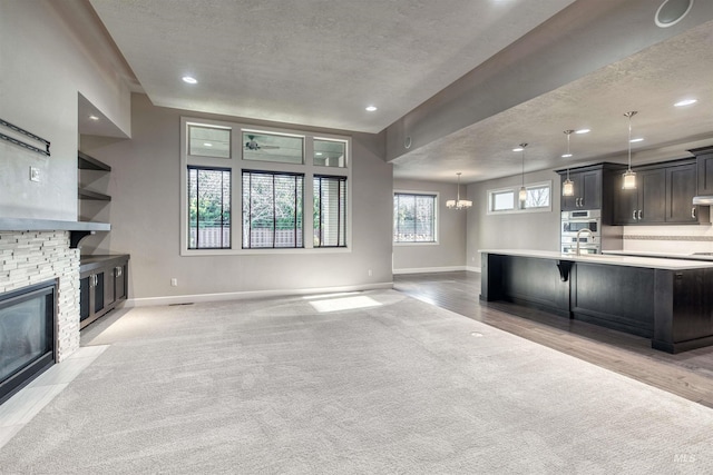 unfurnished living room with a textured ceiling, an inviting chandelier, a stone fireplace, and sink