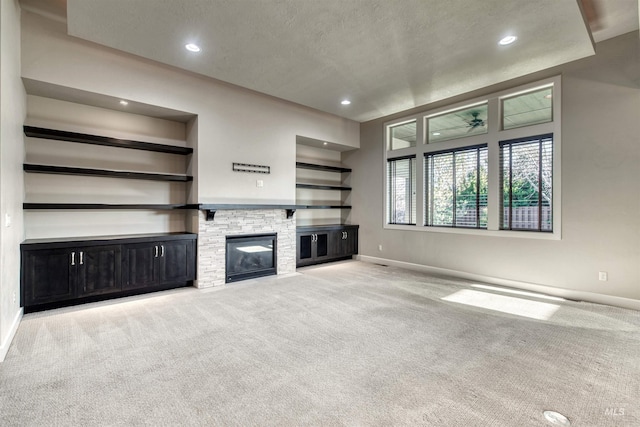 unfurnished living room with built in shelves, a stone fireplace, light colored carpet, and a textured ceiling