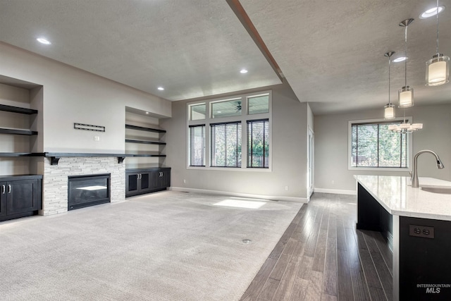 unfurnished living room with sink, dark wood-type flooring, a stone fireplace, built in features, and a textured ceiling