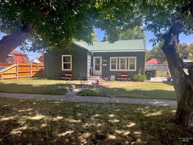 bungalow with a chimney, entry steps, metal roof, fence, and a front lawn