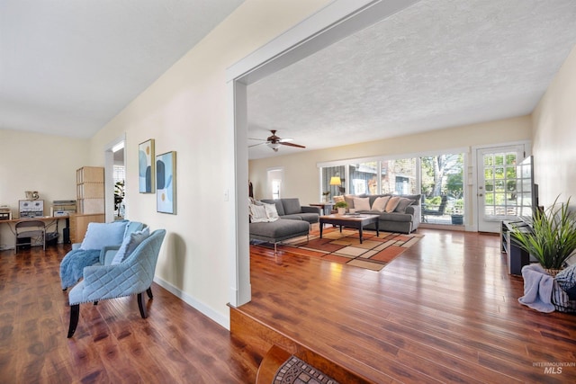 living room featuring wood finished floors, ceiling fan, baseboards, and a textured ceiling