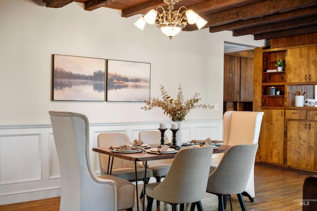 dining area with beam ceiling, a chandelier, wood finished floors, a decorative wall, and a wainscoted wall