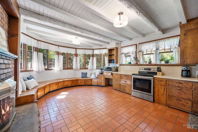 kitchen with appliances with stainless steel finishes, light countertops, brick floors, beam ceiling, and brown cabinets