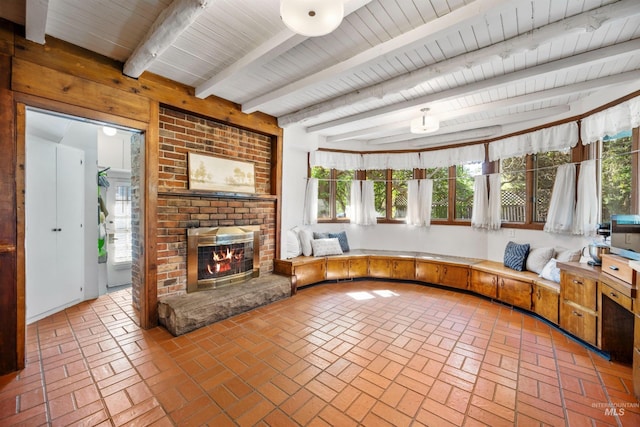 unfurnished living room featuring brick floors, healthy amount of natural light, beam ceiling, a brick fireplace, and wooden ceiling