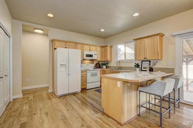 kitchen with light brown cabinetry, a kitchen bar, light hardwood / wood-style floors, kitchen peninsula, and white appliances