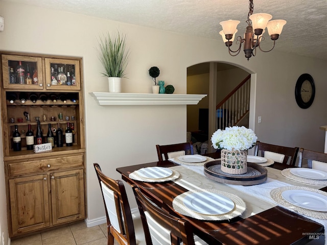 dining space featuring arched walkways, light tile patterned floors, a chandelier, a textured ceiling, and stairs