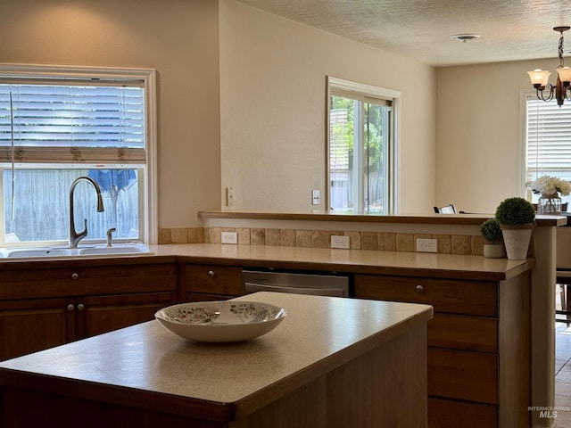 kitchen featuring a sink, stainless steel dishwasher, a kitchen island, a chandelier, and a textured ceiling