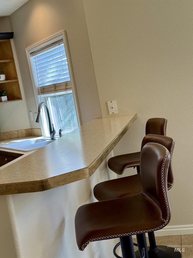 kitchen featuring a sink, a breakfast bar, tile patterned floors, and baseboards
