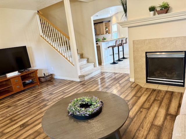 living area with wood finished floors, stairs, baseboards, arched walkways, and a tiled fireplace