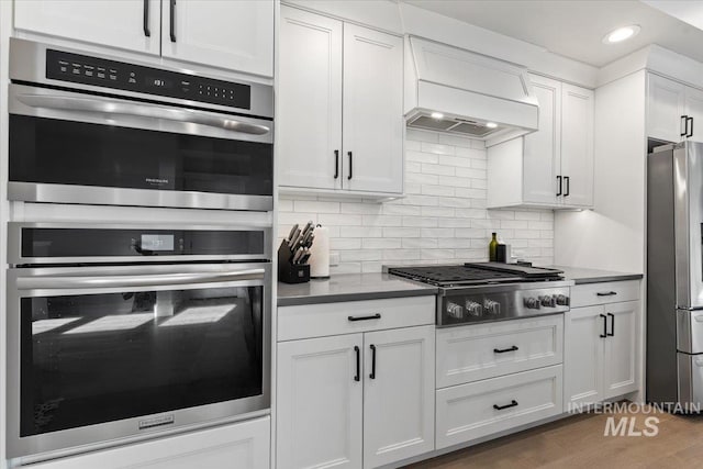 kitchen featuring tasteful backsplash, white cabinets, custom range hood, and appliances with stainless steel finishes