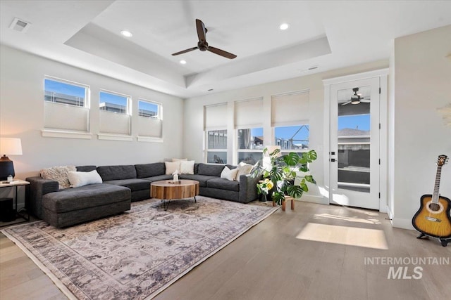 living room featuring wood-type flooring, a tray ceiling, and ceiling fan