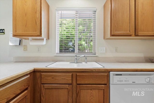 kitchen featuring dishwasher, a sink, light countertops, and brown cabinetry