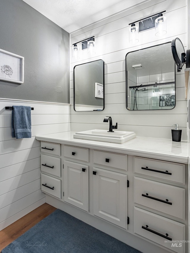 bathroom featuring hardwood / wood-style flooring, vanity, wooden walls, and a textured ceiling