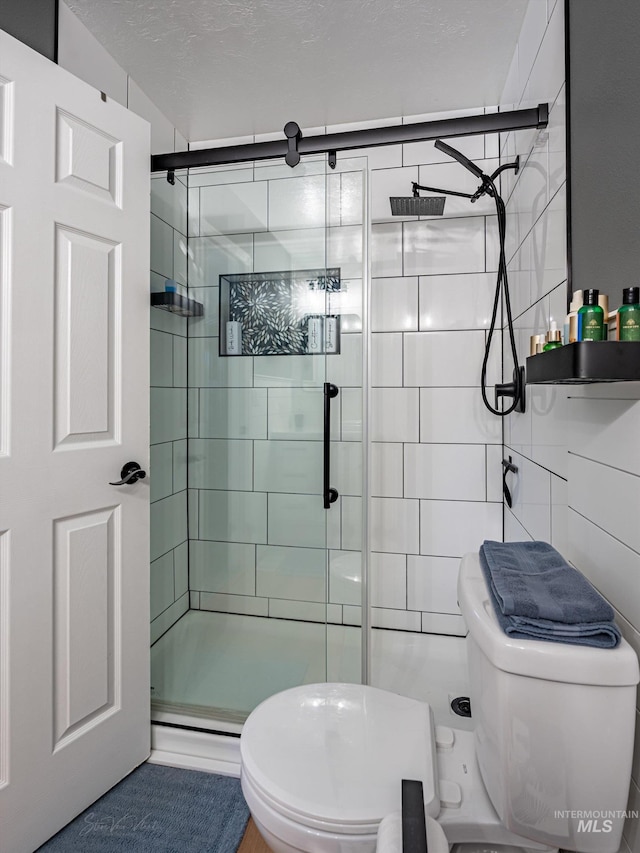 bathroom featuring toilet, a shower with door, tile walls, and a textured ceiling