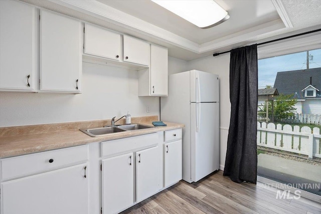 kitchen featuring freestanding refrigerator, light wood-type flooring, light countertops, white cabinets, and a sink