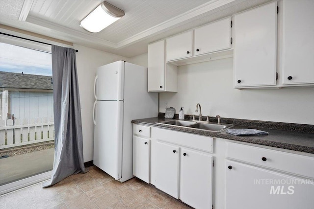 kitchen featuring freestanding refrigerator, dark countertops, a sink, and white cabinets
