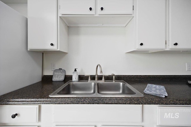 kitchen with a sink, dark countertops, and white cabinetry