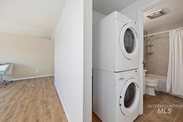 washroom featuring laundry area, a textured ceiling, stacked washer / dryer, visible vents, and light wood finished floors