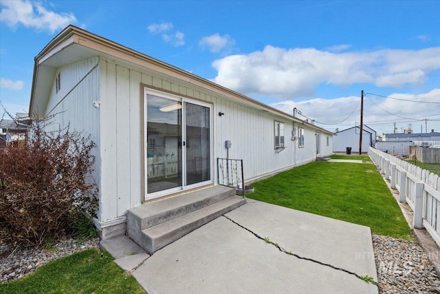 rear view of property with entry steps, fence, a lawn, and a patio area
