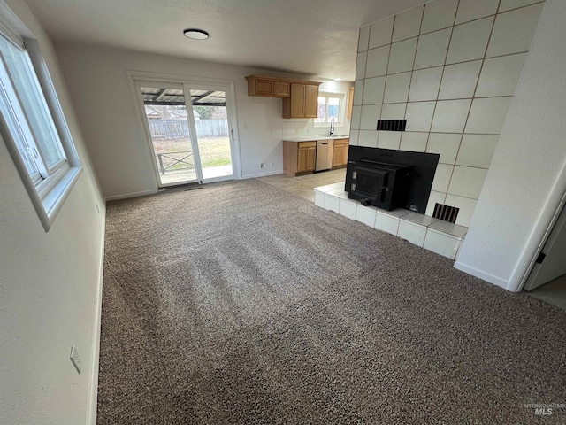 unfurnished living room featuring light carpet, a wood stove, baseboards, and a sink