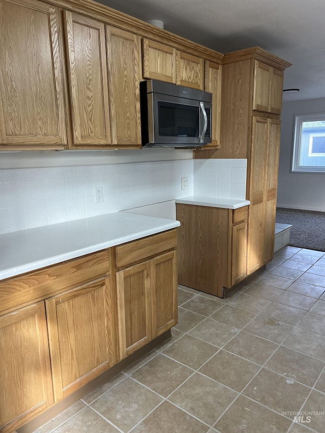 kitchen with stainless steel microwave, light countertops, light tile patterned floors, decorative backsplash, and brown cabinetry