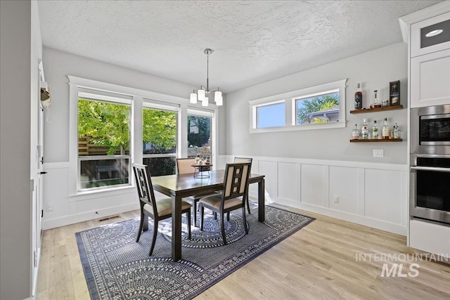 1753 S Kimball Way, Boise, ID 83709 - dining space with light wood-style floors, a textured ceiling, a chandelier, a decorative wall, and wainscoting