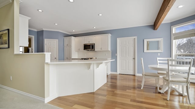 kitchen with light countertops, stainless steel microwave, light wood-style flooring, backsplash, and white cabinets