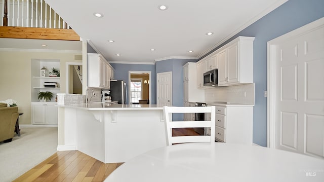 kitchen featuring a breakfast bar, appliances with stainless steel finishes, ornamental molding, white cabinets, and a peninsula