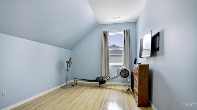 exercise area featuring baseboards, visible vents, vaulted ceiling, and wood finished floors