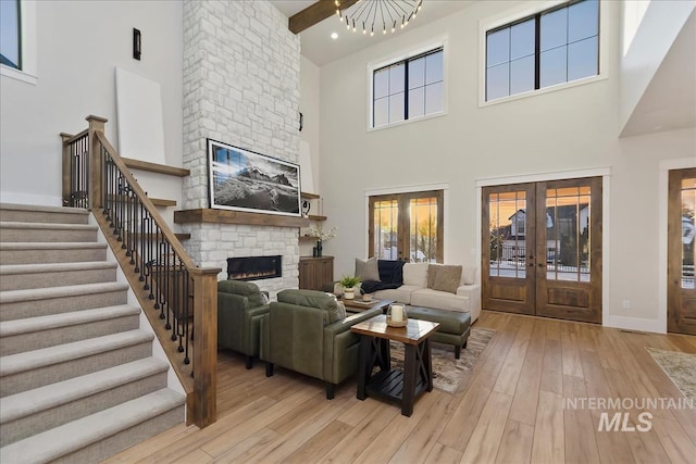 living room with french doors, a fireplace, beam ceiling, and light hardwood / wood-style flooring