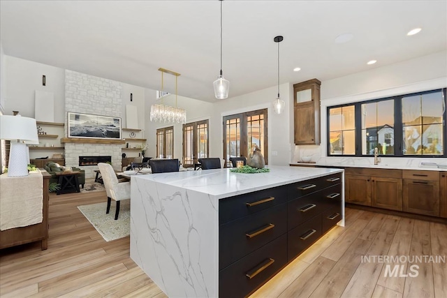 kitchen with a center island, a fireplace, light stone countertops, decorative light fixtures, and light wood-type flooring