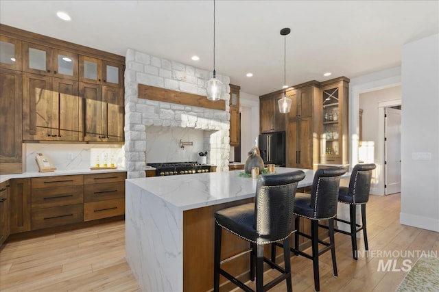 kitchen featuring a kitchen bar, hanging light fixtures, high quality fridge, stainless steel gas stovetop, and a kitchen island with sink