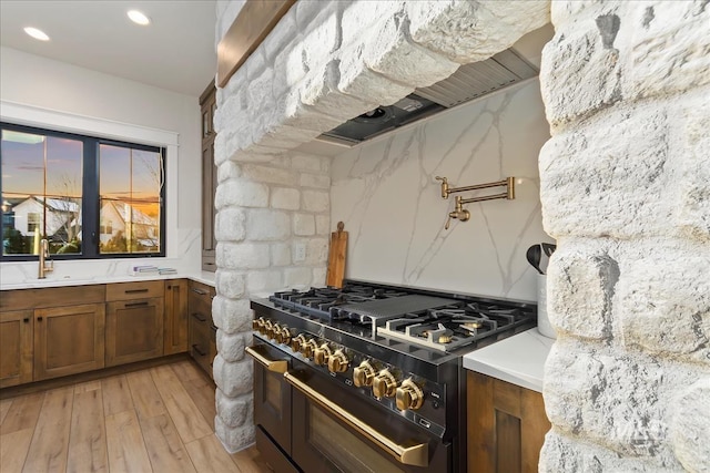 kitchen with light stone counters, sink, light wood-type flooring, and range with two ovens